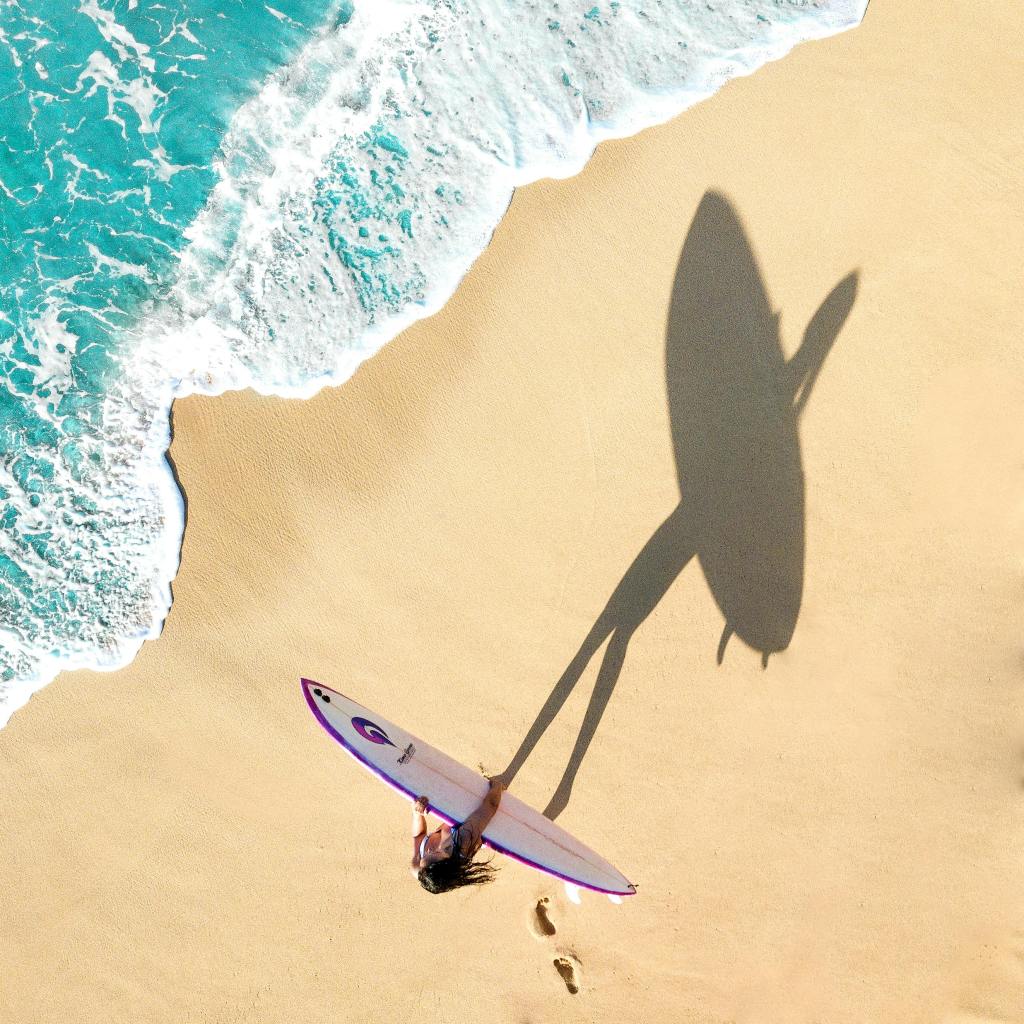 woman walking on seashore with white and purple surf board